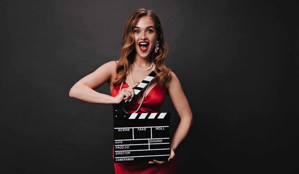 mujer de rojo con rostro feliz y sonriente mientras sujeta una claqueta de cine