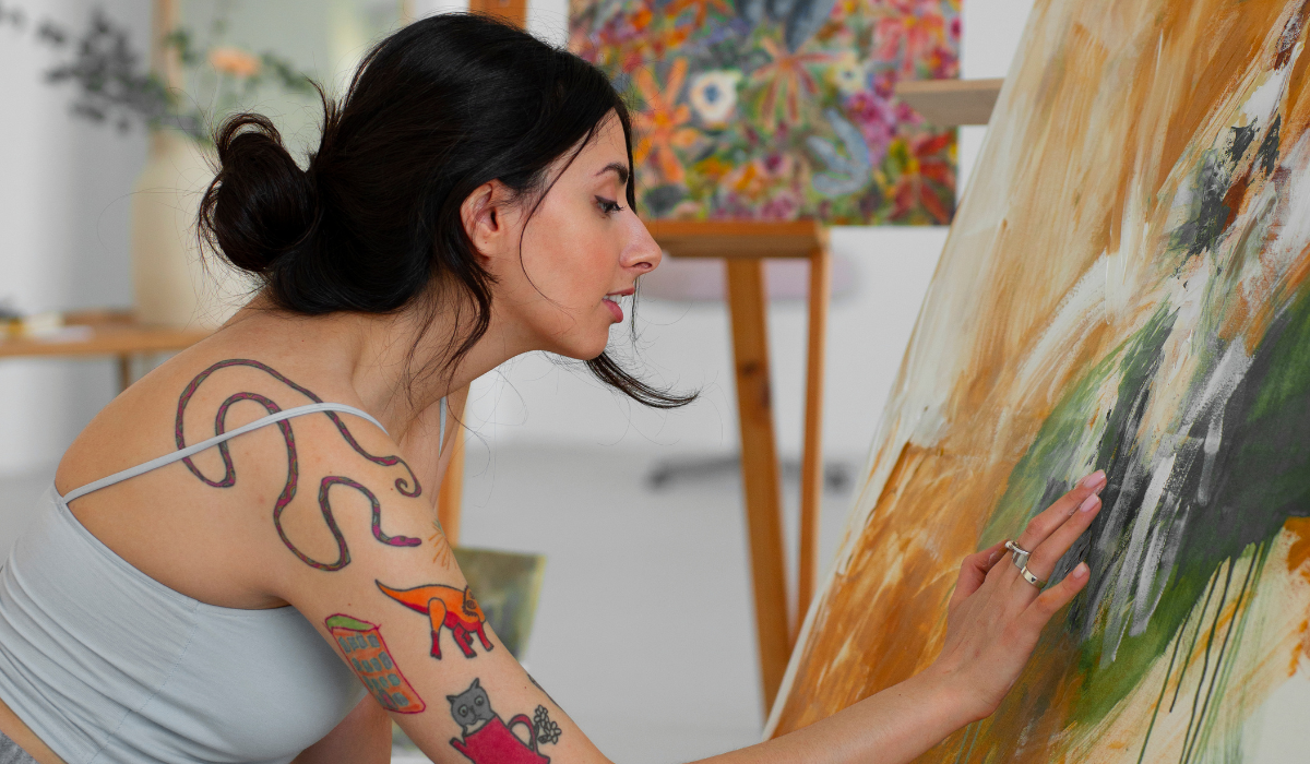 mujer morena con tatuajes pintando un cuadro dentro de su casa, con el pelo recogido en un moño